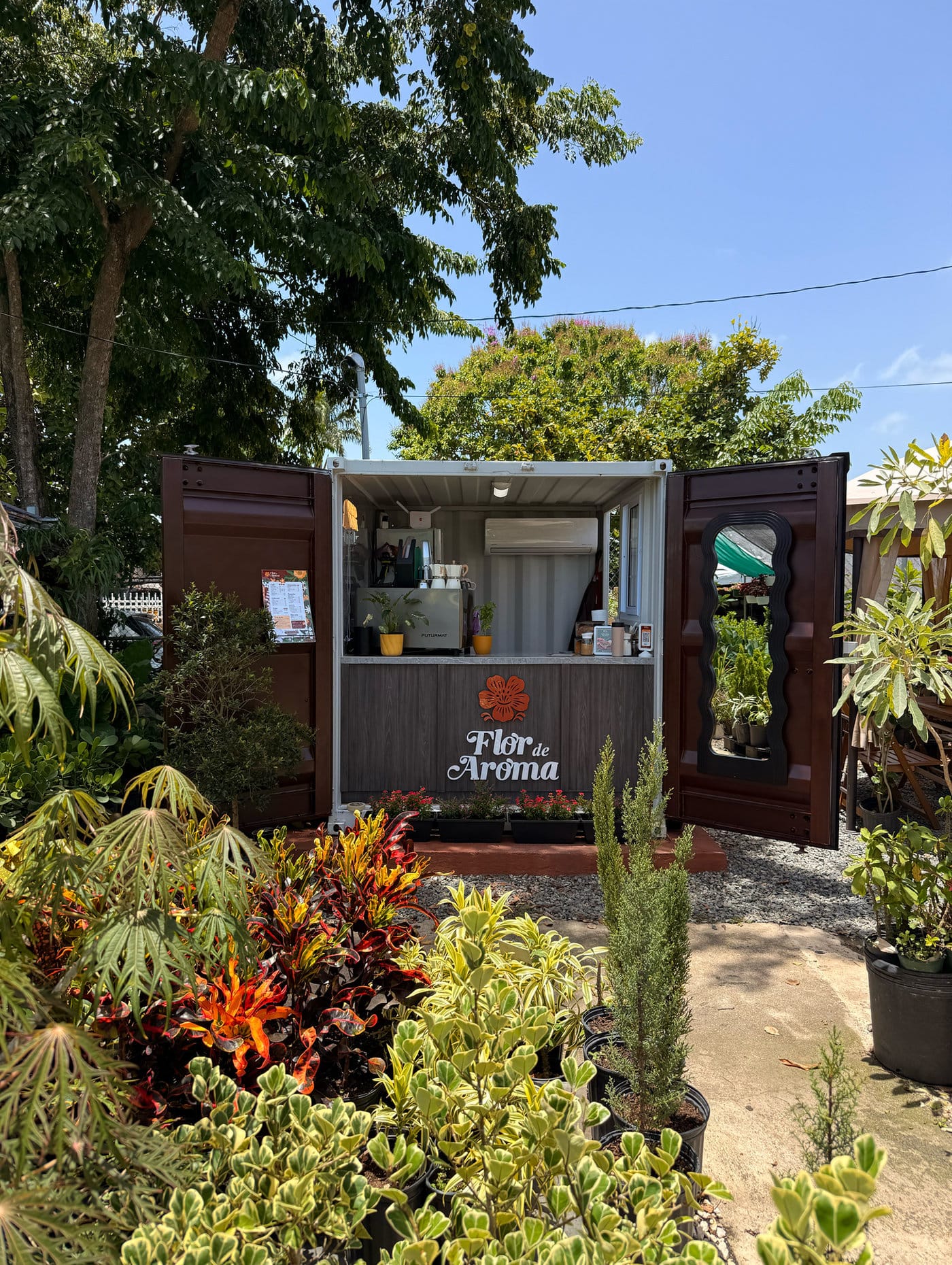 El contenedor de Flor de Aroma con las puertas abiertas, rodeado de plantas del Jardín de Carmencita